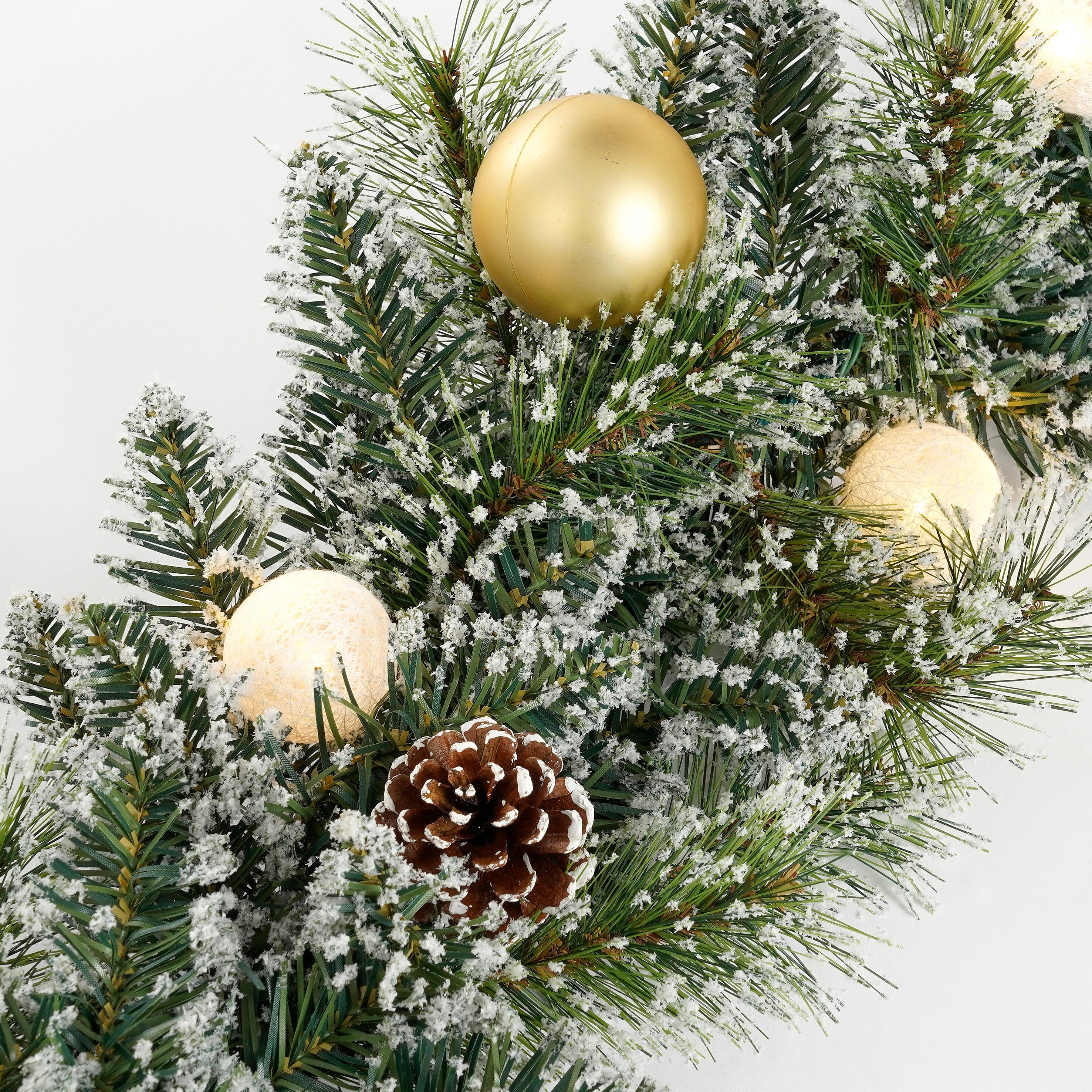 Verschneiter Tannenzweig mit Goldkugel, Zapfen und warmen Lichterketten.
