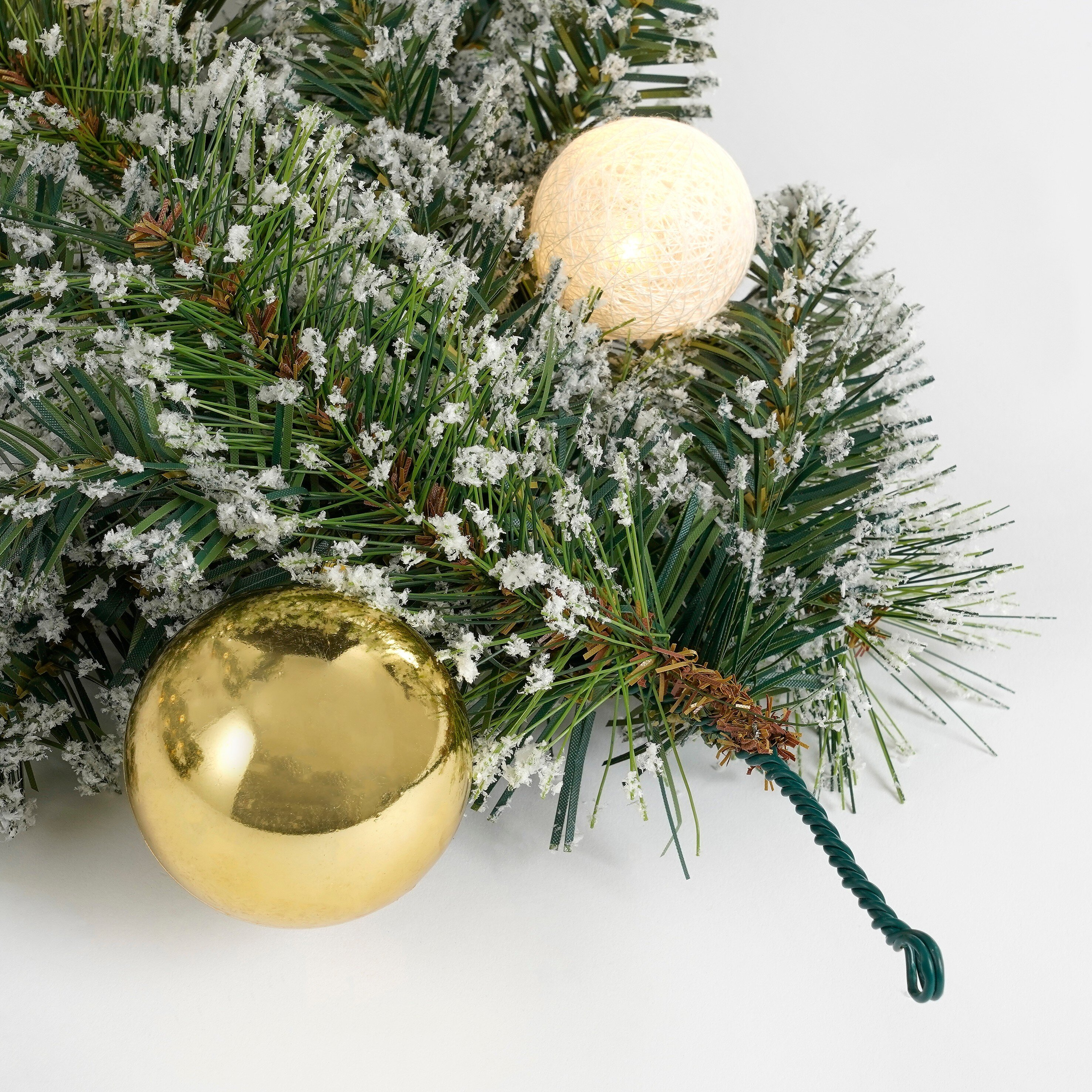 Verschneiter Tannenzweig mit einer goldenen Kugel und einer beleuchteten Ballleuchte auf weißem Hintergrund.