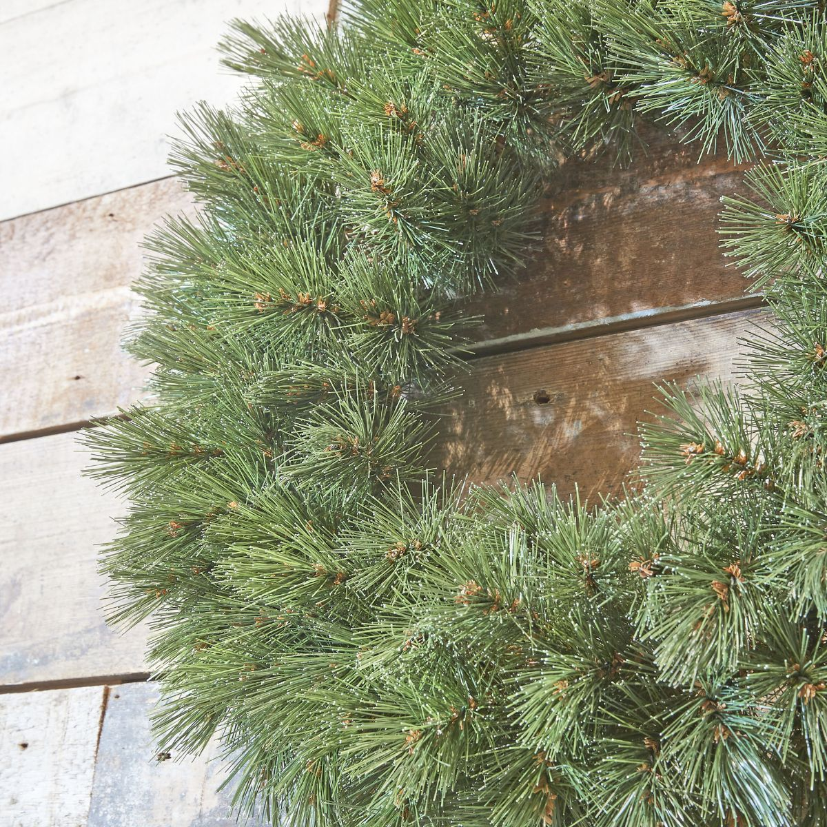 A green pine wreath hangs on a rustic wooden wall.