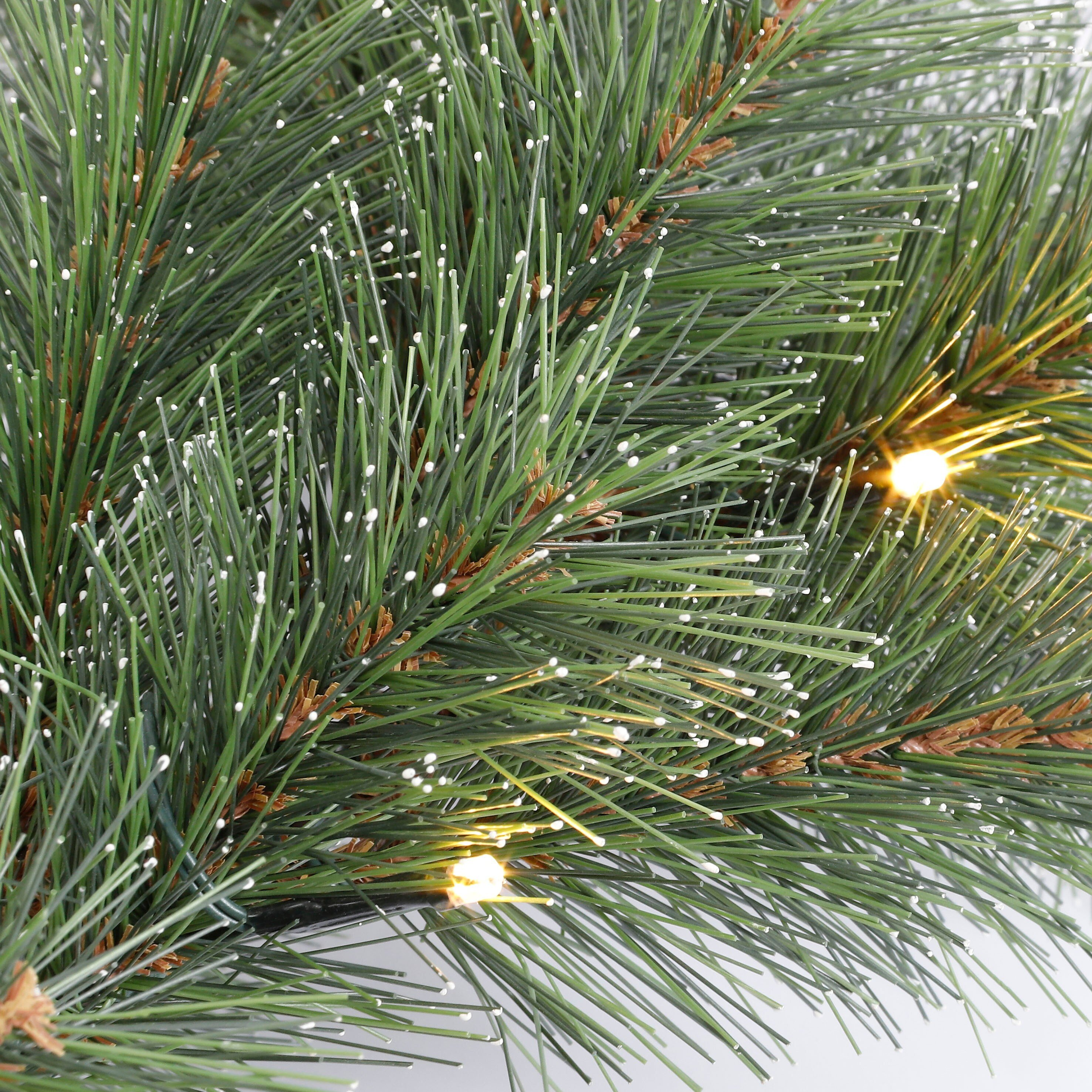 Grüne Tannennadeln mit künstlichem Schnee und warmen Lichterketten.
