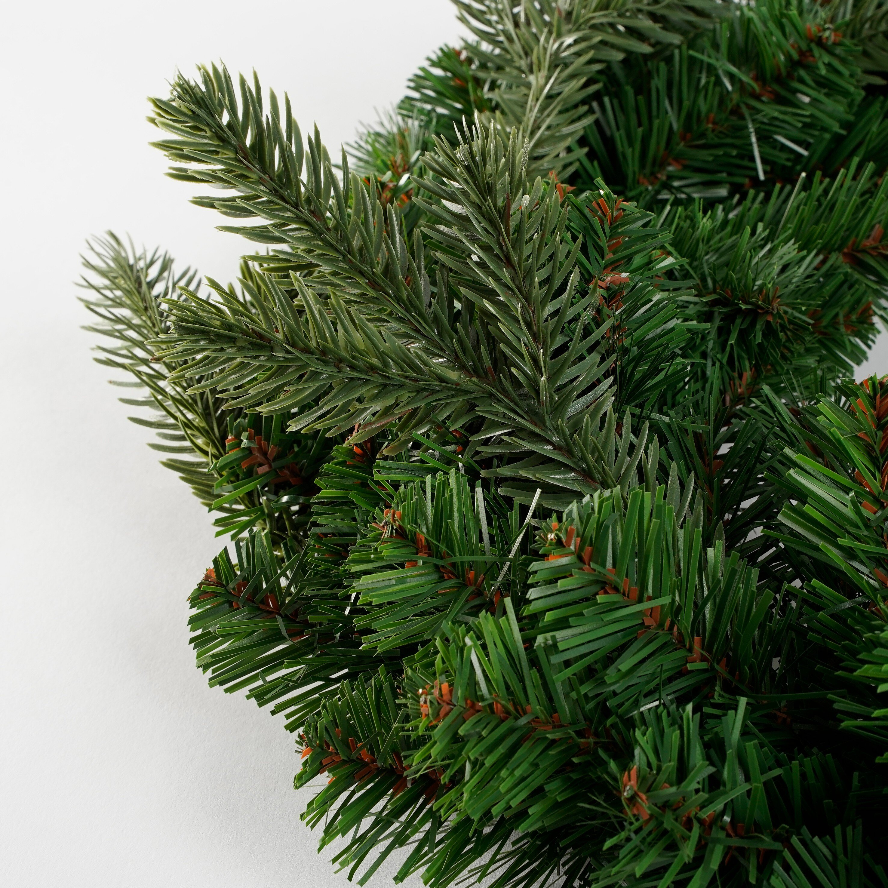Gros plan de branches de pin vertes artificielles sur fond blanc.