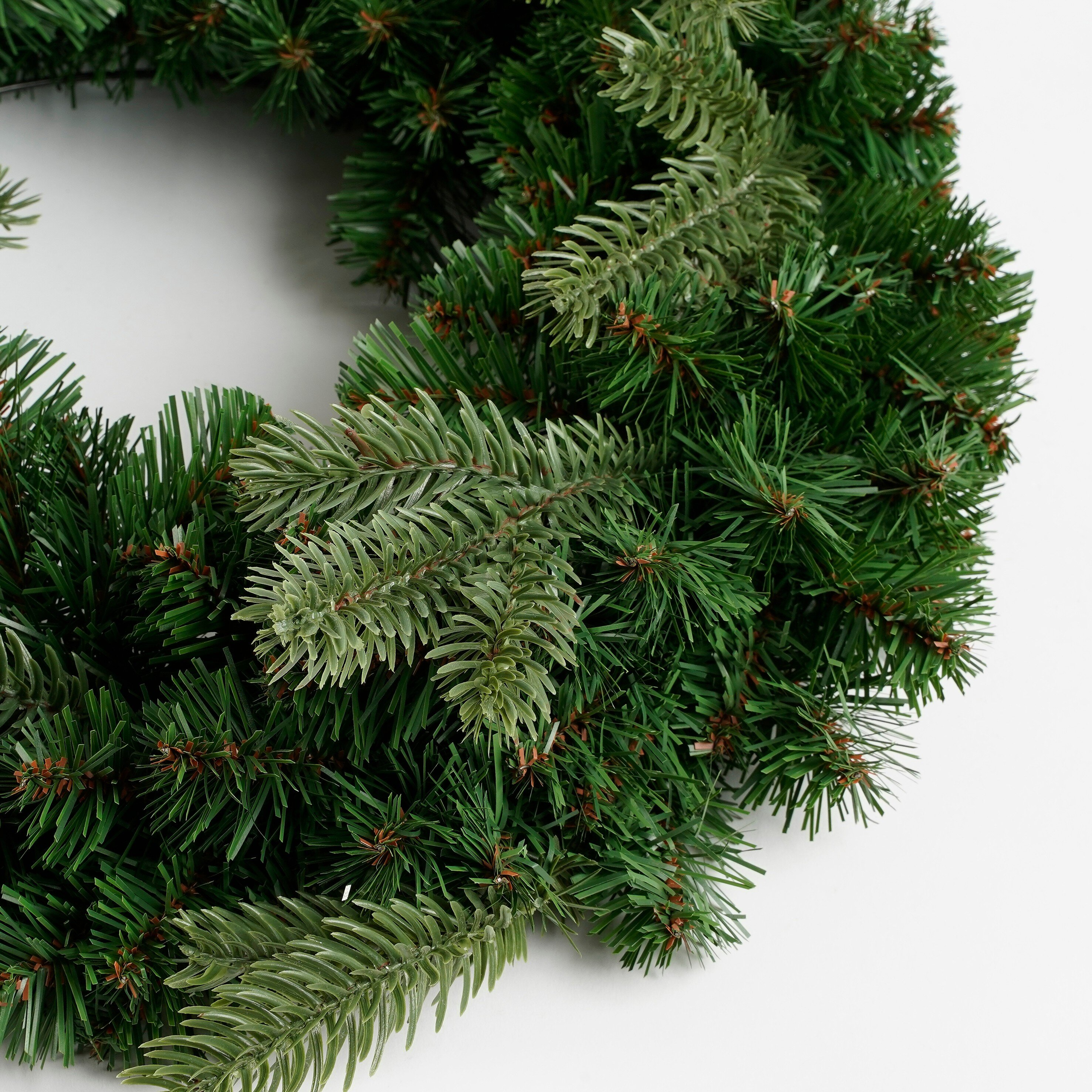 Une couronne de Noël en pin artificiel vert sur fond blanc.