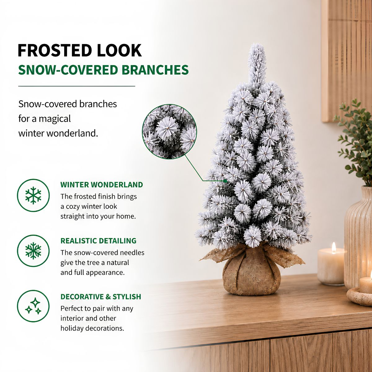 A small frosted Christmas tree with a burlap base stands on a wooden table, next to lit candles.