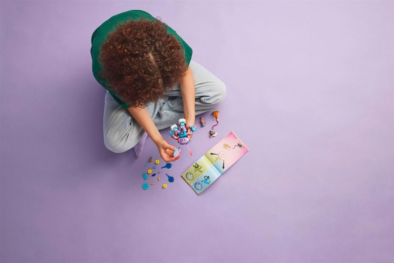 Ein Kind mit lockigen Haaren sitzt auf einer lila Oberfläche und baut mit kleinen Spielzeugen.