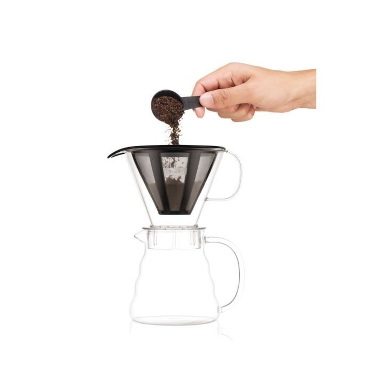 Eine Hand schüttet Kaffeemehl aus einem Löffel in den Filter einer Glas-Kaffeekanne.