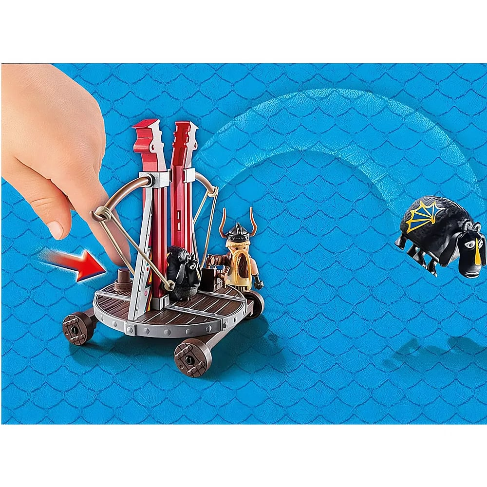 Eine Hand zieht eine Spielzeug-Katapult-Falle ab, während ein fliegendes Schaf über einen blauen Hintergrund fliegt.