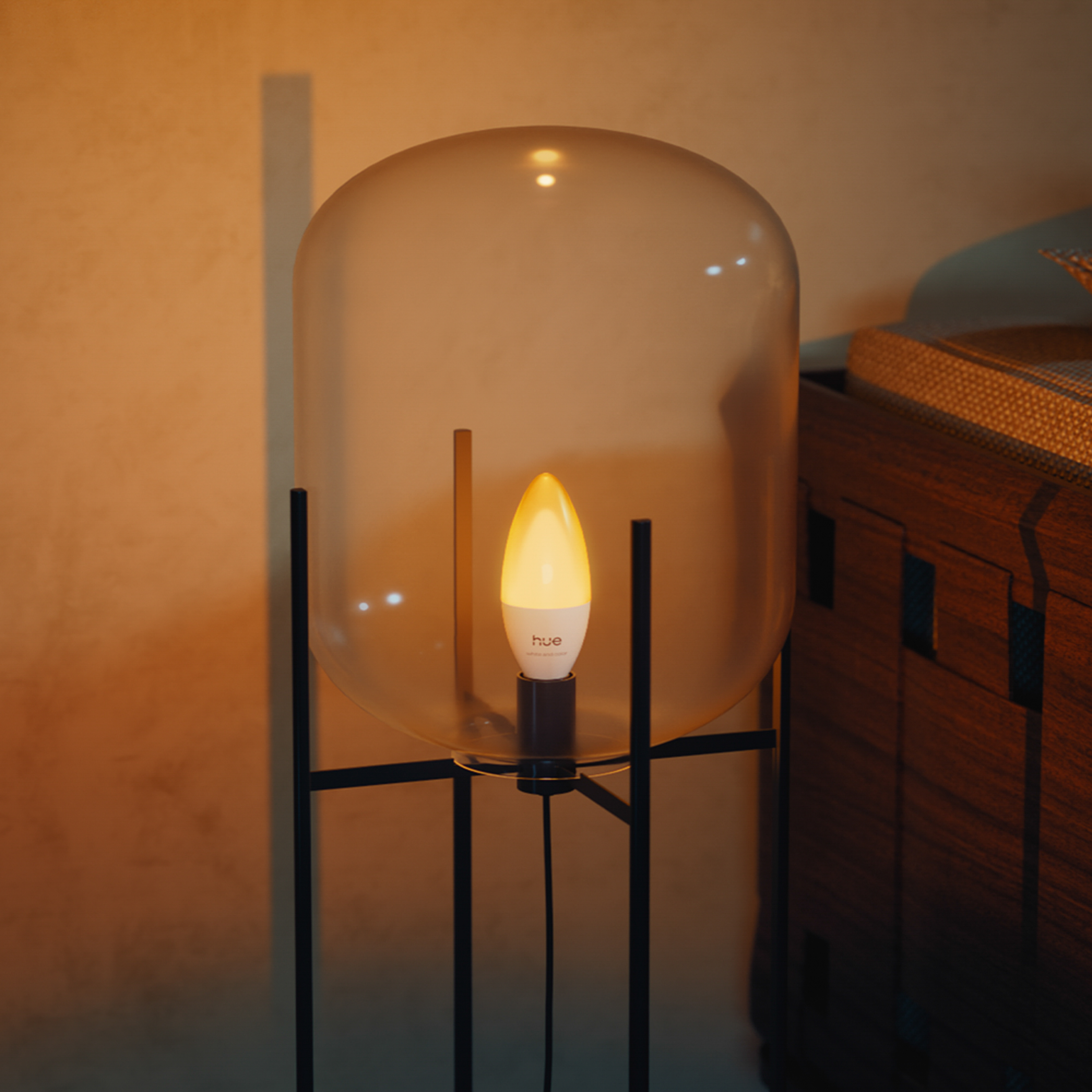 Eine moderne Glaskuppel-Stehlampe mit einer warm leuchtenden Philips Hue Kerzenlampe auf schwarzem Metallgestell.