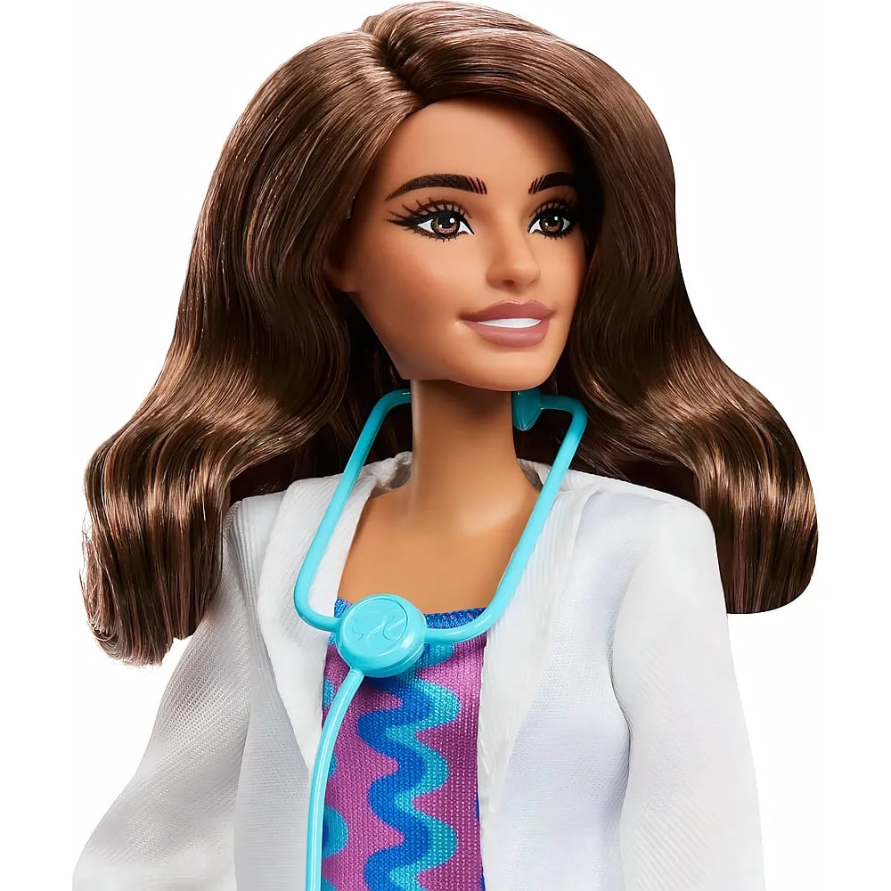 Una muñeca castaña vestida de médico con bata blanca y estetoscopio azul.