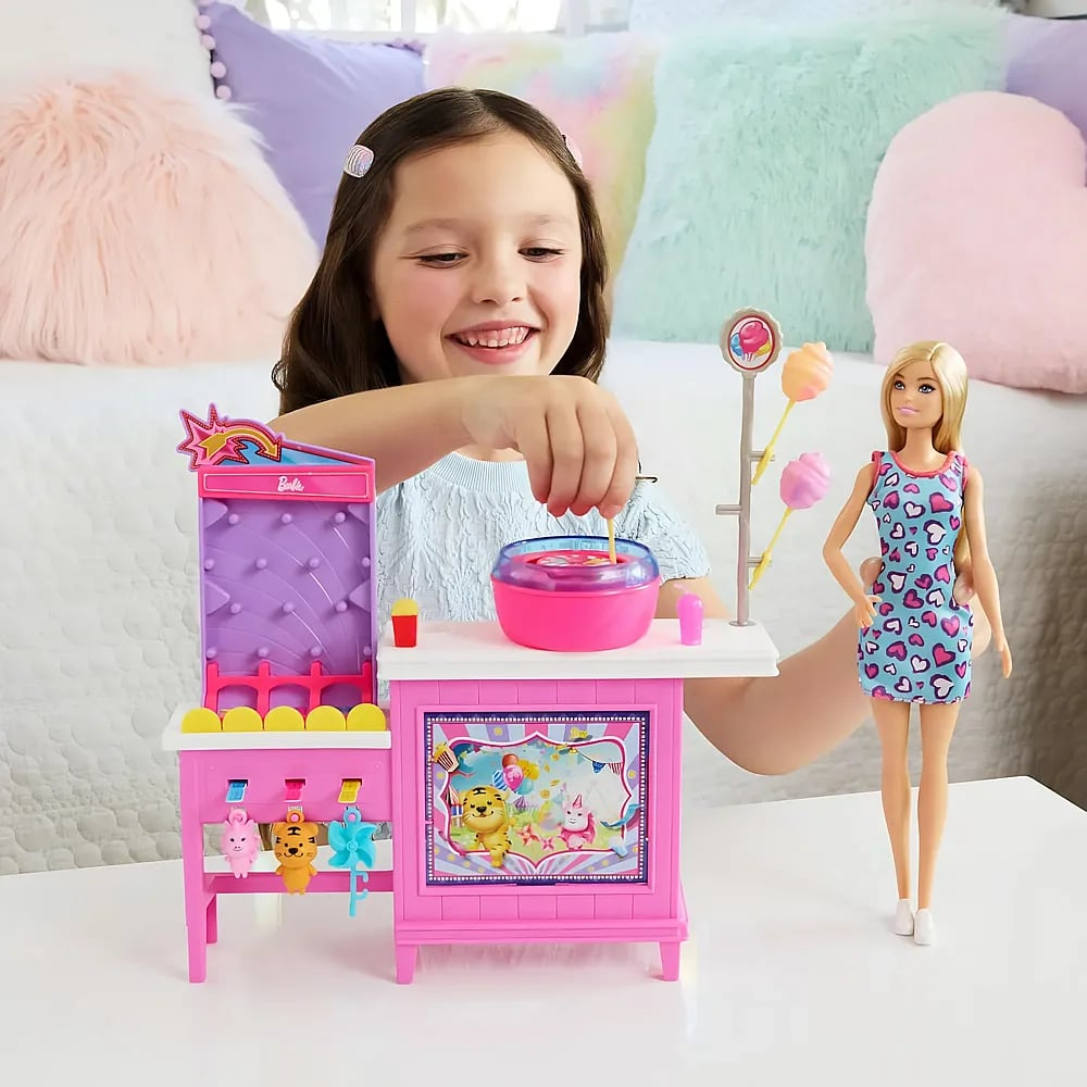 Ein junges Mädchen lächelt, während sie mit einem Barbie-Spielset mit Karnevalsthema und einer Puppe spielt.