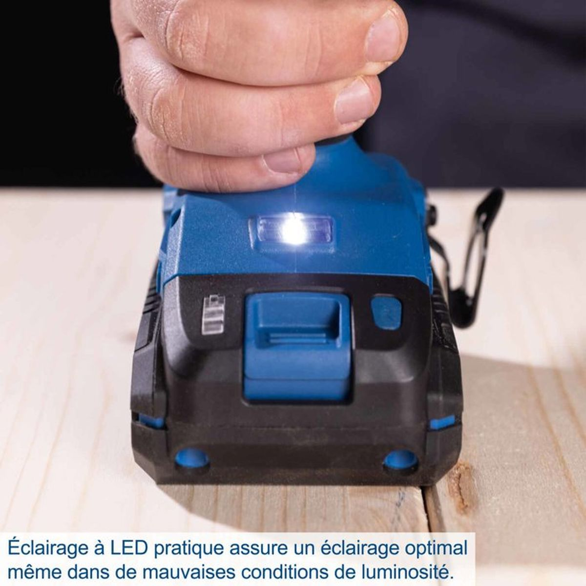Eine Hand hält eine blaue Akku-Bohrmaschine mit eingeschalteter LED-Leuchte über einem Holztisch.