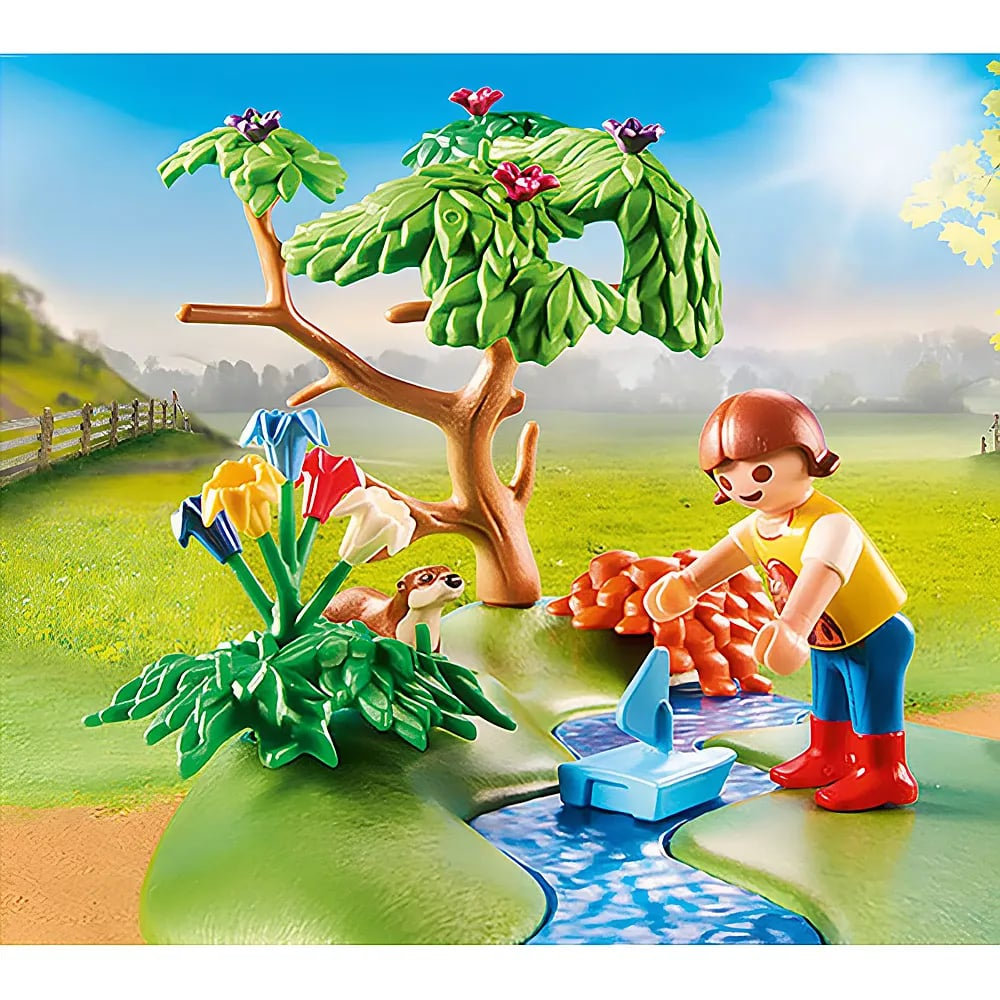 Playmobil-Figur spielt am Bach mit einem Boot, neben Blumen, einem Baum und einem Otter.