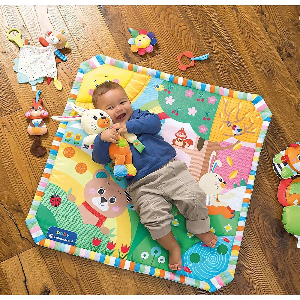 Un bambino felice sdraiato su un tappeto gioco colorato abbraccia un peluche.