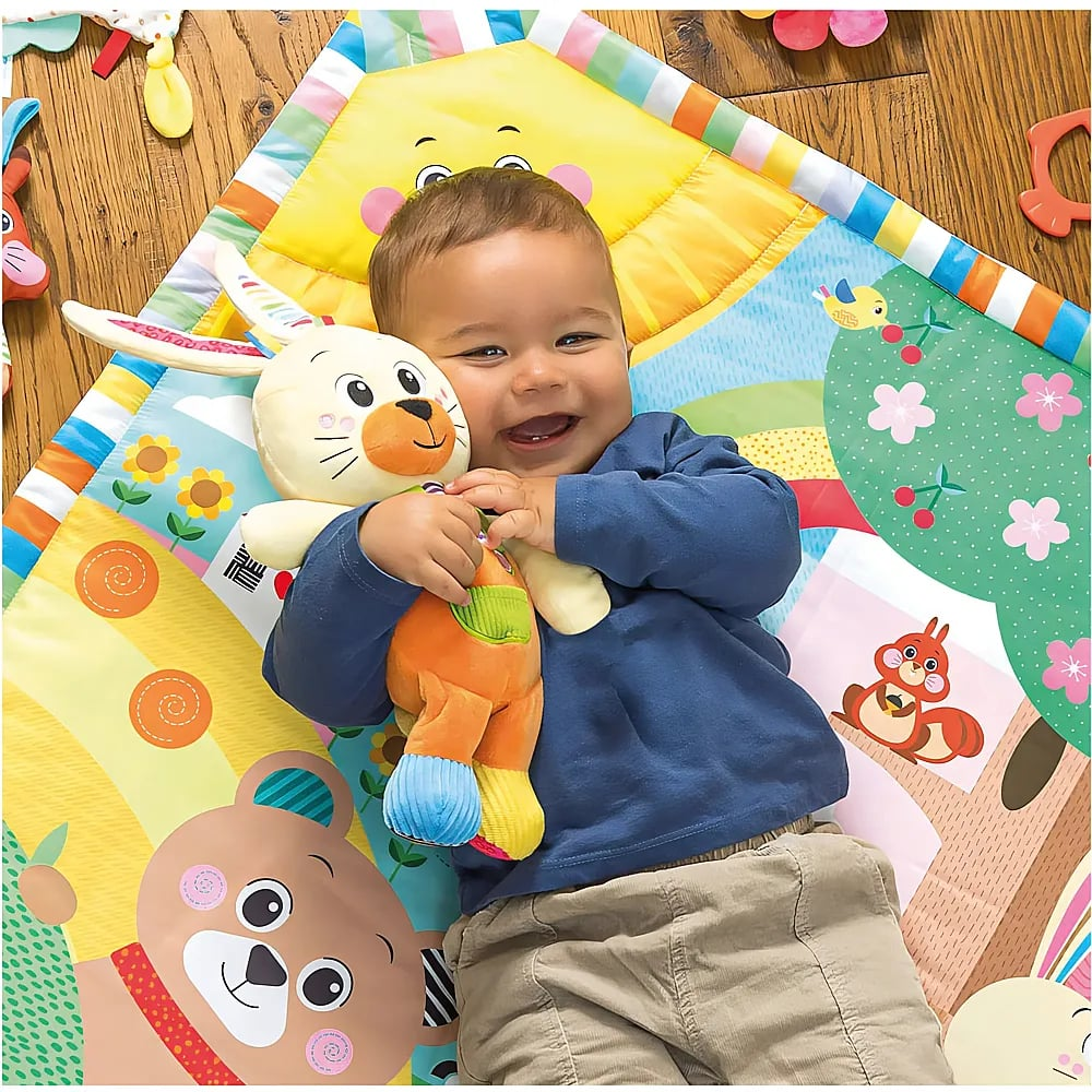 Un bambino felice è sdraiato su un tappeto gioco colorato e abbraccia un peluche.