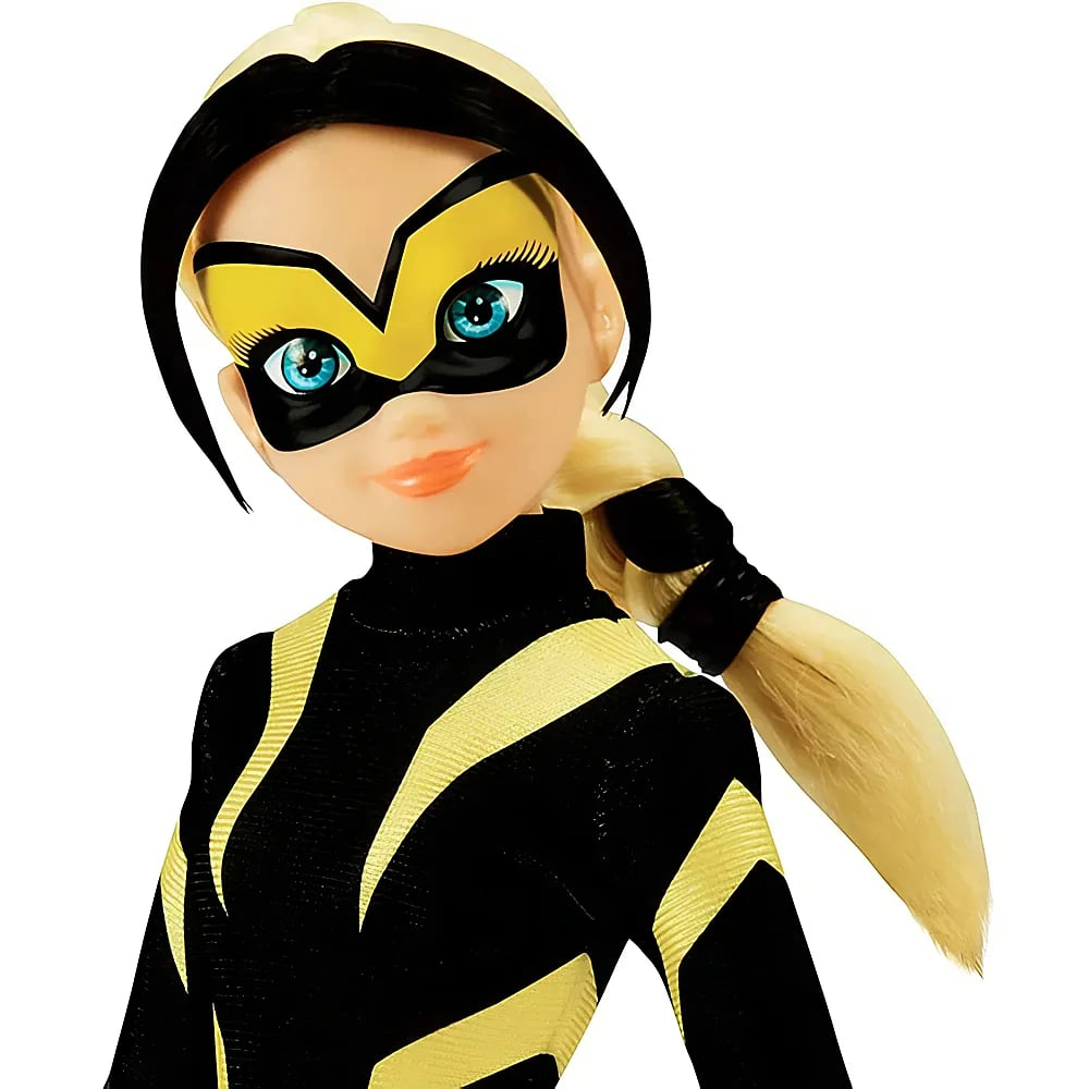 Eine blonde Puppe mit einer schwarz-gelben Superheldenmaske und passendem Anzug vor weißem Hintergrund.
