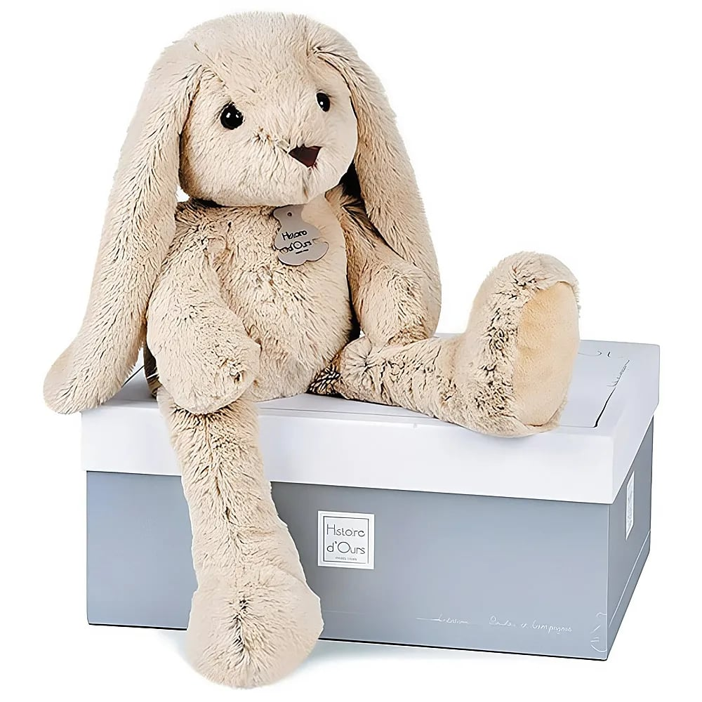 Ein flauschiger, beiger Plüschhase sitzt auf einer weiß-grauen Geschenkbox.