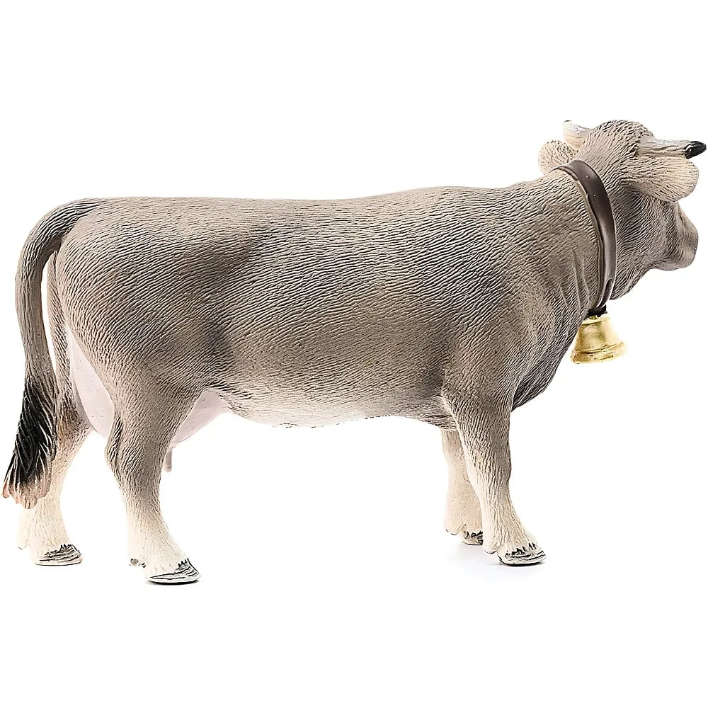 Eine graue Spielzeugkuh mit weißem Bauch und einer Glocke um den Hals steht auf weißem Grund.