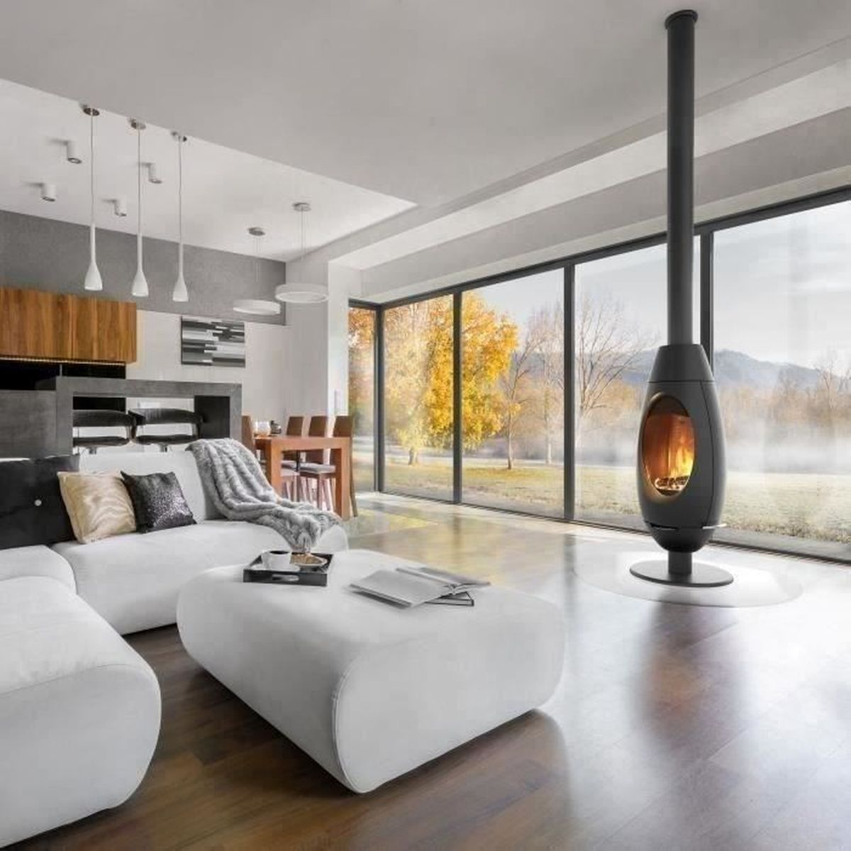 Ein modernes Wohnzimmer mit weißem Sofa, schwarzem Kamin und großen Fenstern mit Blick ins Grüne.