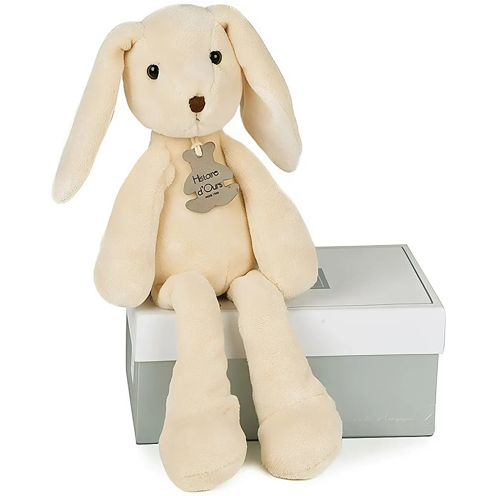 Un coniglietto di peluche beige con le orecchie lunghe siede su una scatola grigia e bianca su sfondo bianco.