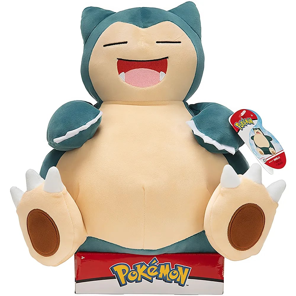 Ein sitzender Plüsch-Snorlax mit breitem Lächeln sitzt auf einer Pokémon-Box.