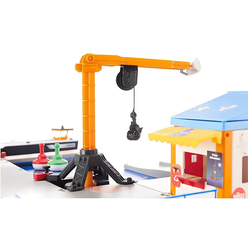 Ein orangener Spielzeugkran steht vor einem Gebäude mit blauem Dach und roten und grünen Markierungen auf der Oberfläche.