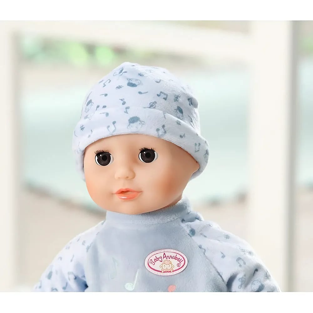 Eine Babypuppe mit blauer Mütze und blauem Strampler vor hellem Hintergrund.