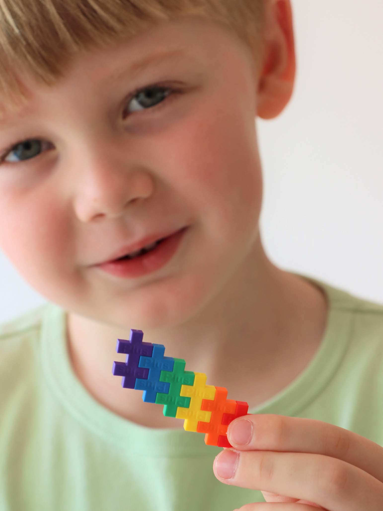 Un bambino sorride tenendo in mano un giocattolo di costruzione colorato fatto di pezzi a incastro.