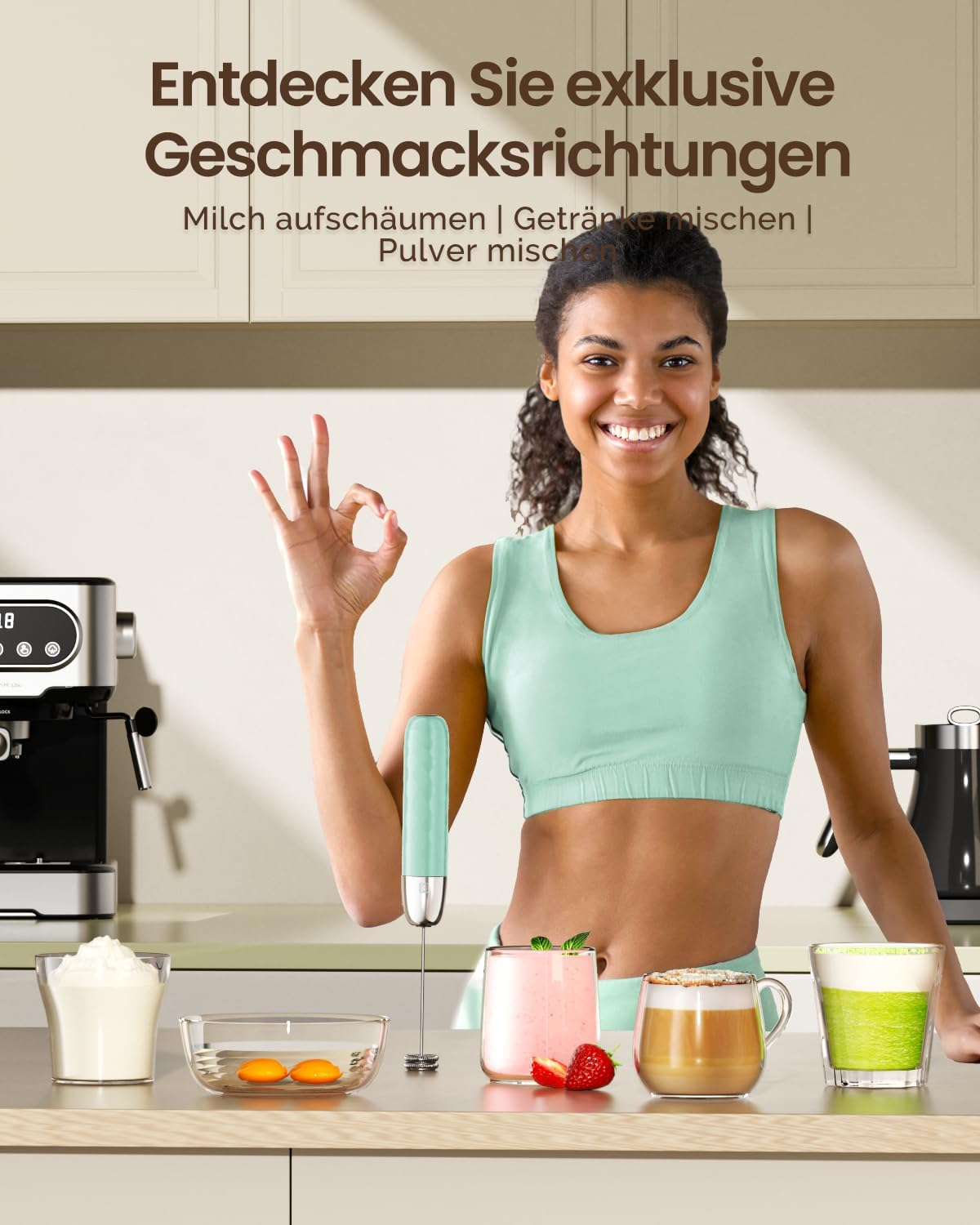 Eine lächelnde Frau macht ein O-Zeichen in einer Küche mit einem Milchaufschäumer und Getränken auf dem Tisch.