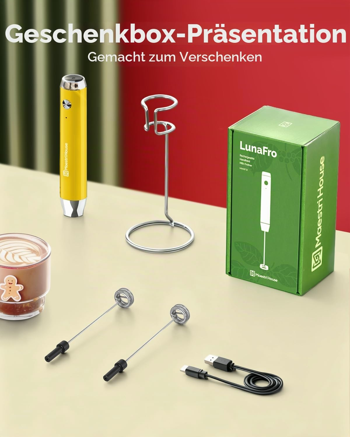 Gelber Milchaufschäumer, grüner Karton, Metallständer, Whisk-Aufsätze und USB-Kabel auf beigeem Tisch.