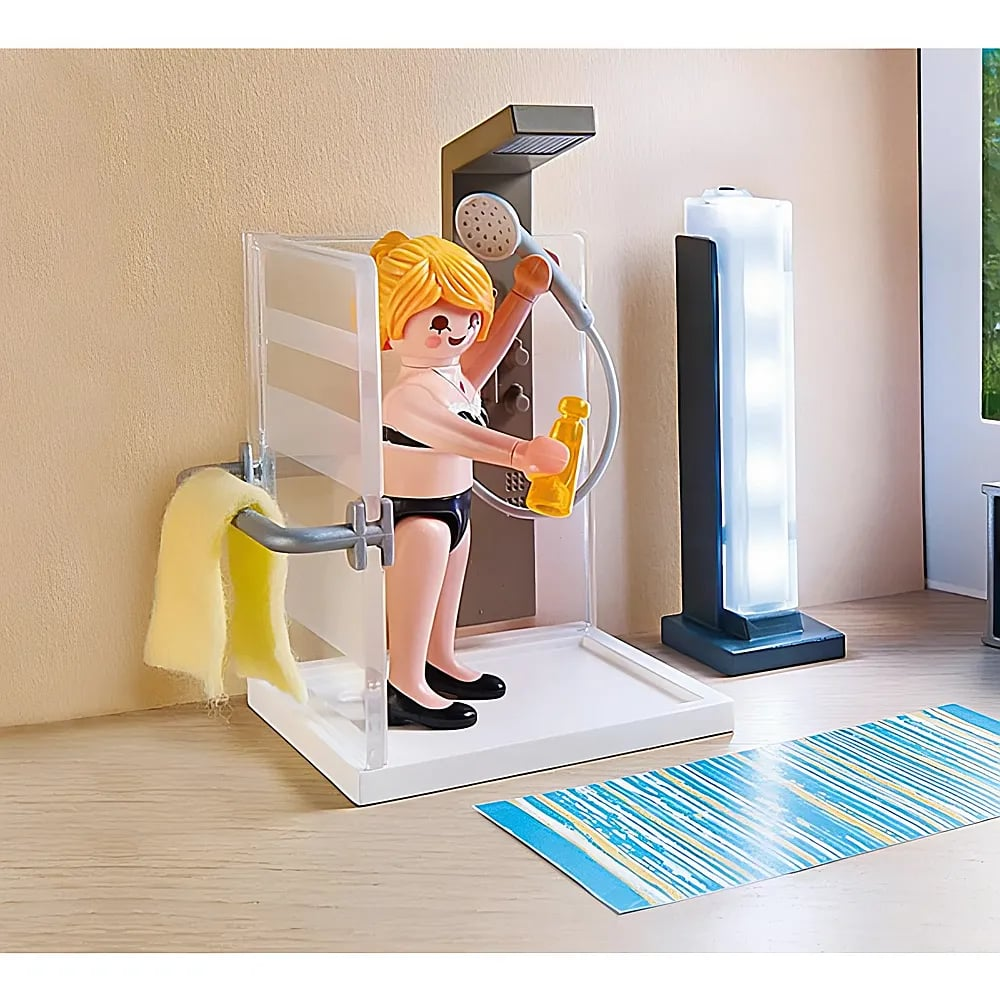 Eine Playmobil-Figur in einem Duschset aus Plastik mit gelber Flasche, gelbem Handtuch und blau-weißem Bademattengewebe.