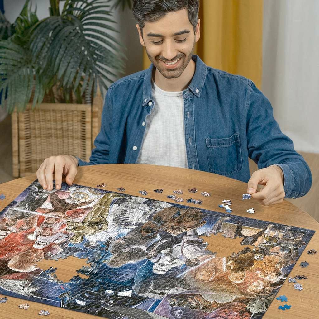 Ein lächelnder Mann sitzt an einem Holztisch und setzt ein großes Star Wars-Puzzle zusammen.
