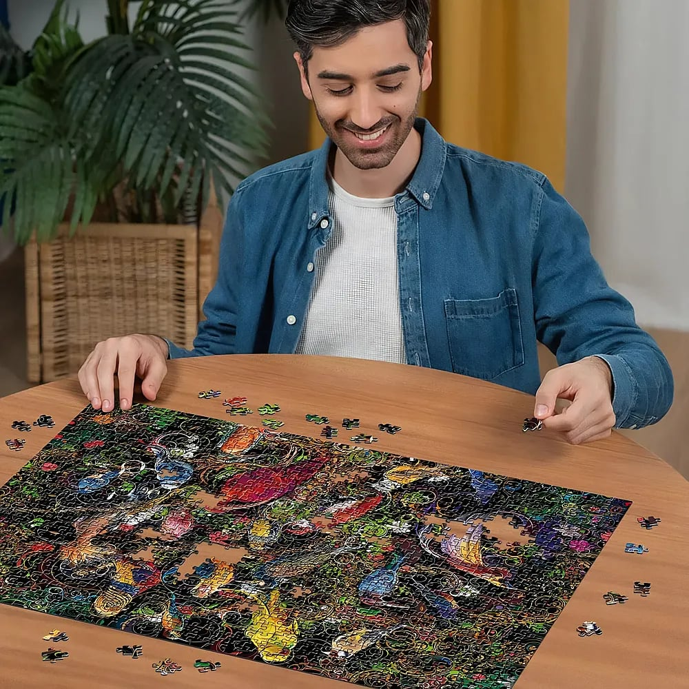 Ein lächelnder Mann in blauem Hemd sitzt an einem Holztisch und löst ein buntes Puzzle.