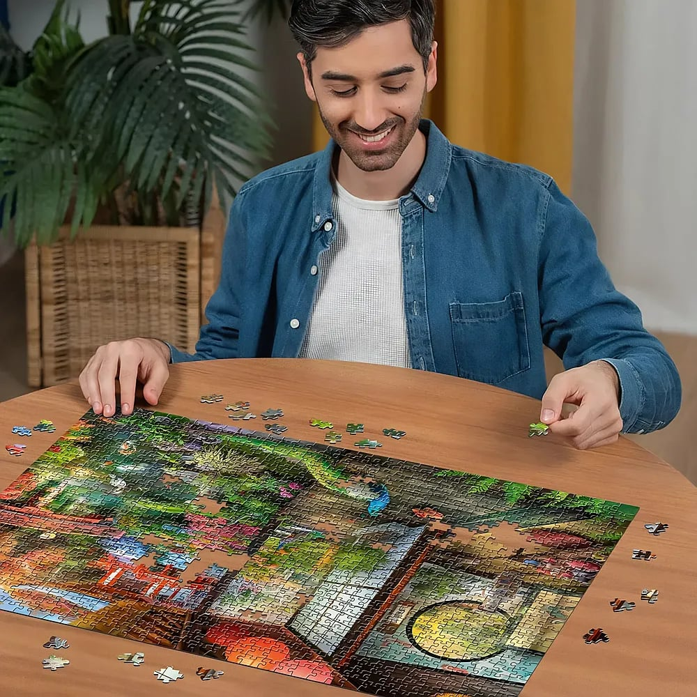 Un hombre sonriente está sentado en una mesa de madera armando un rompecabezas grande y colorido.