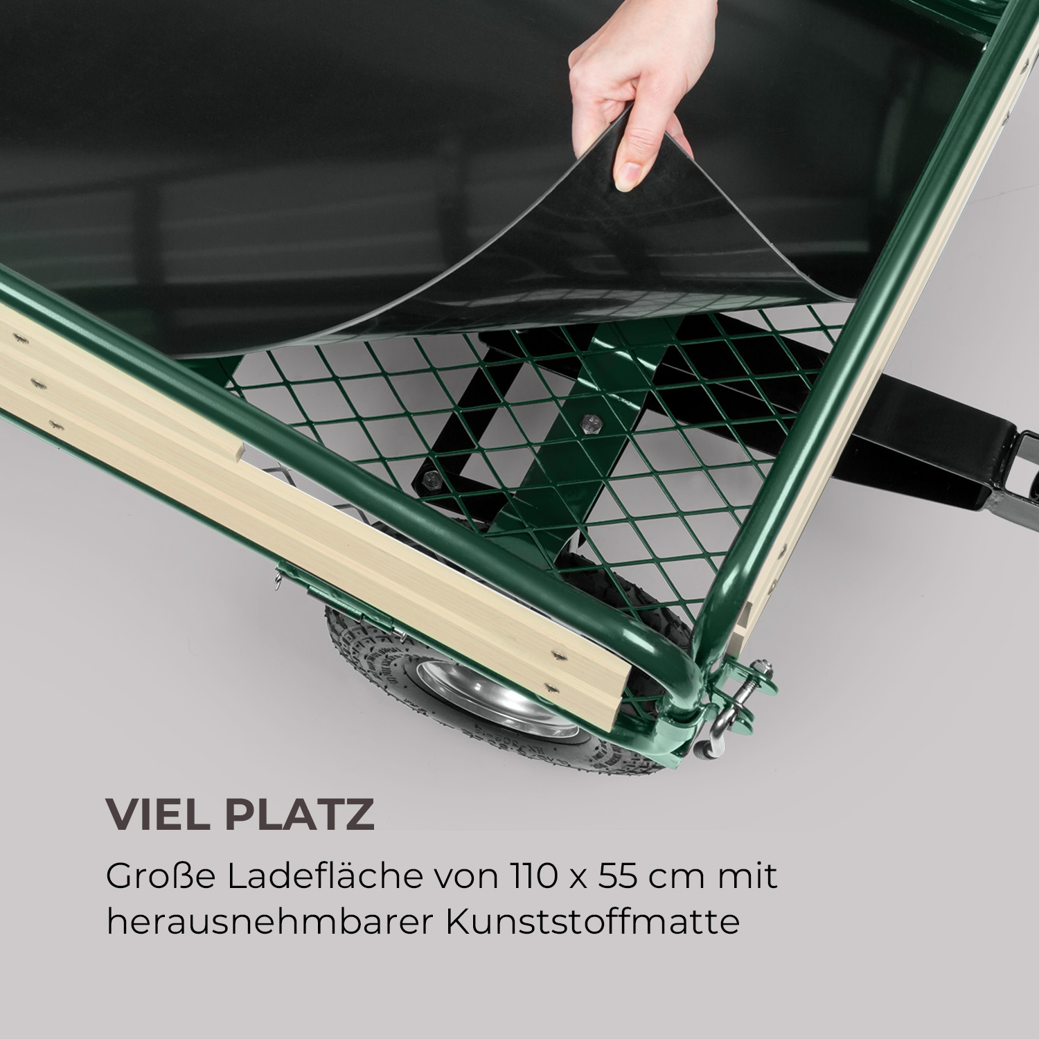 Hand lüftet eine schwarze Matte aus dem grünen Gartenwagen mit Gitterboden heraus.