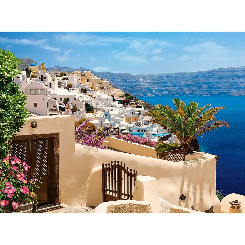 Weiße Häuser und eine blaue Kuppel auf einer Klippe in Santorin mit Blick auf das blaue Meer und Palmen.