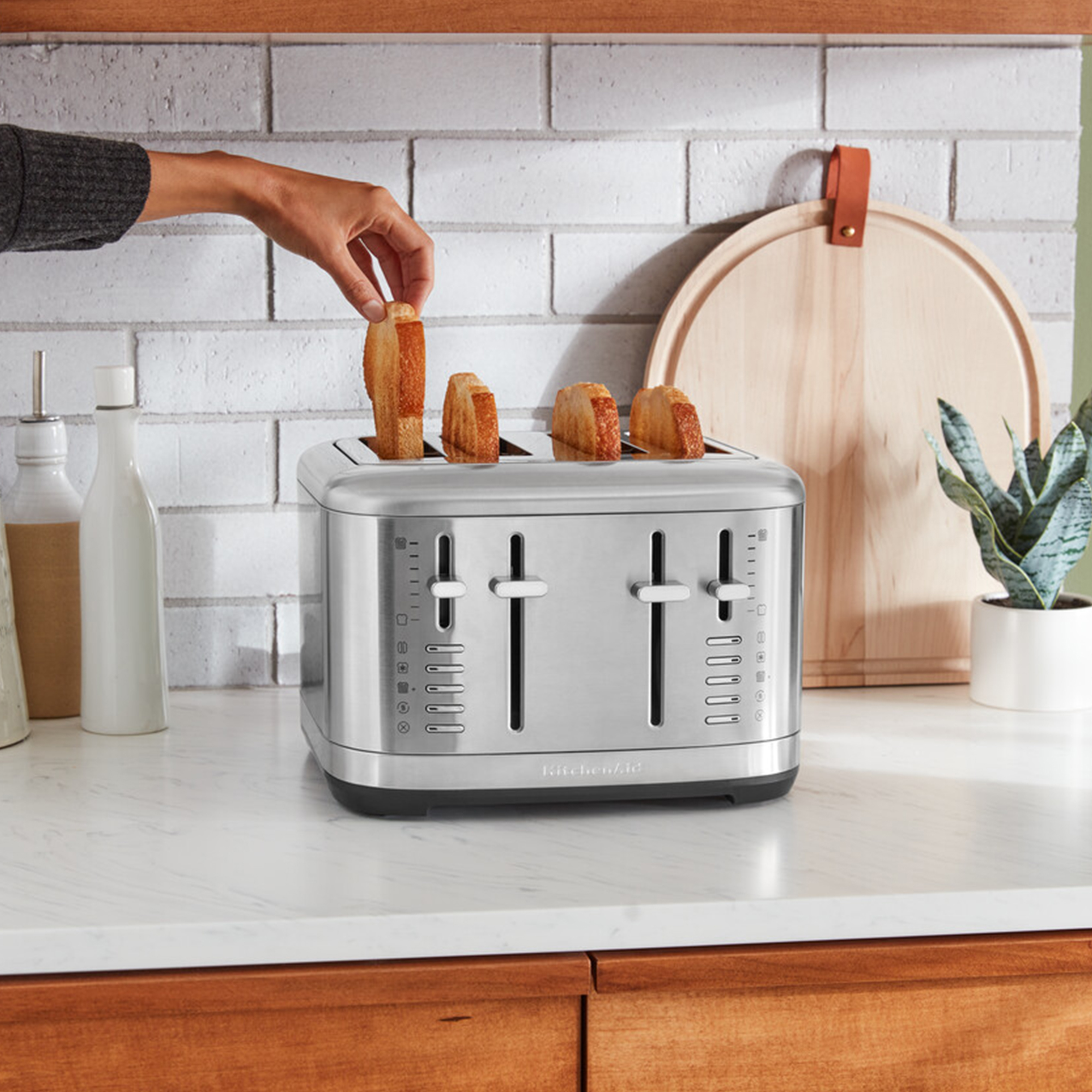 Eine Hand legt eine Scheibe Toastbrot in einen Edelstahl-Vier-Scheiben-Toaster auf einer Küchentheke.
