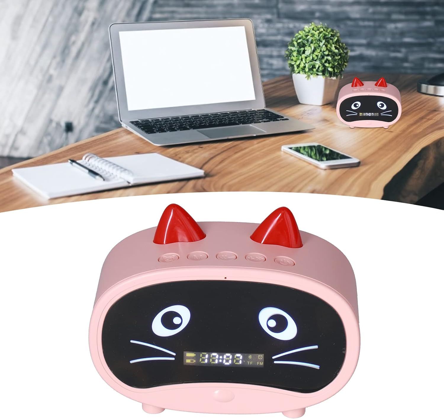 Ein rosa katzenförmiger Digitalwecker mit roten Hörnern steht auf einem Holztisch mit Laptop und Notizbuch.