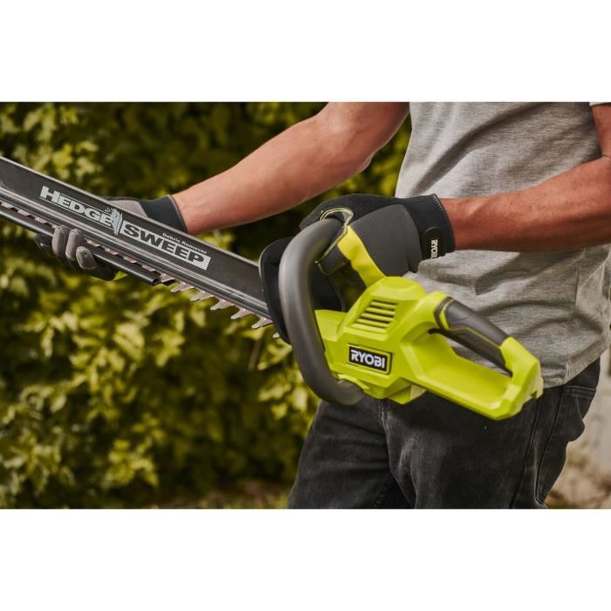 Person hält eine grüne Ryobi-Heckenschere mit Hedge Sweep-Aufsatz vor Büschen.