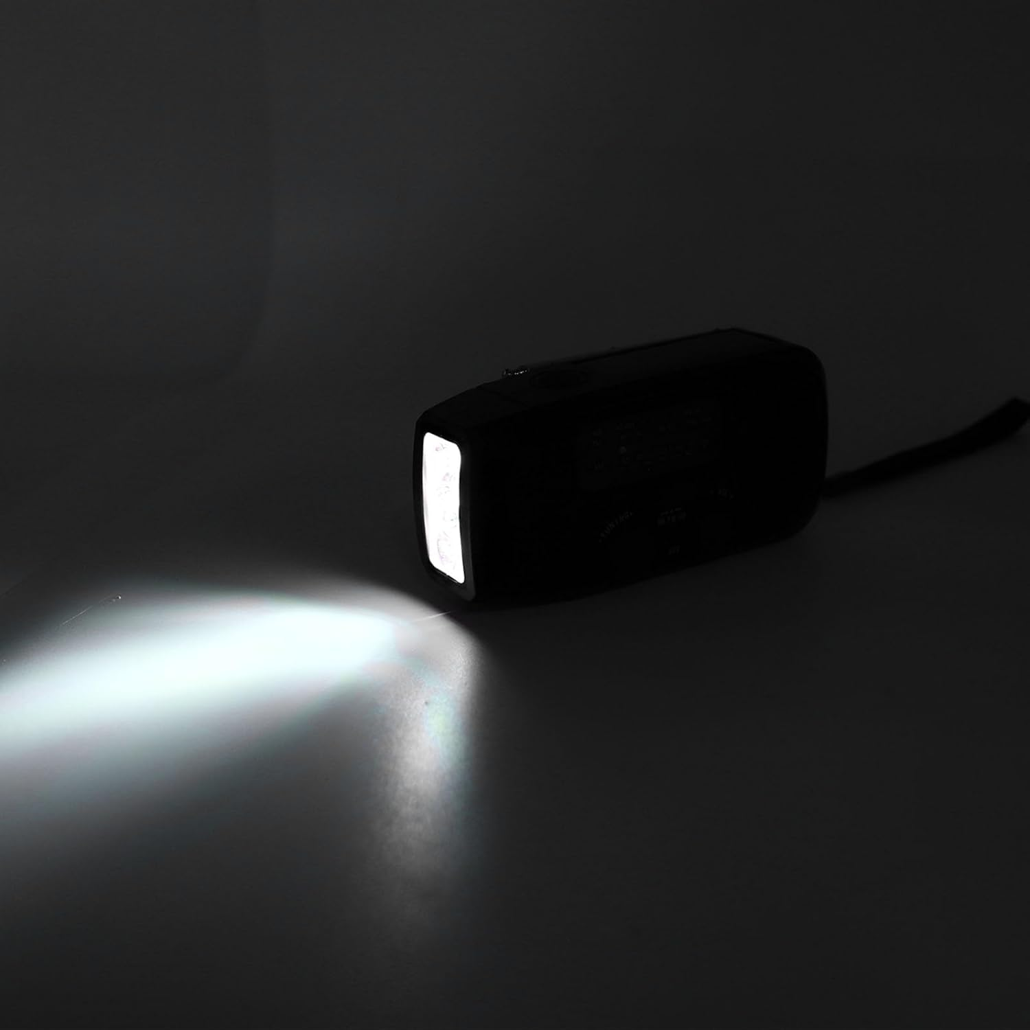 Eine schwarze Taschenlampe leuchtet in einem dunklen Raum und wirft einen hellen Lichtkegel auf den Boden.