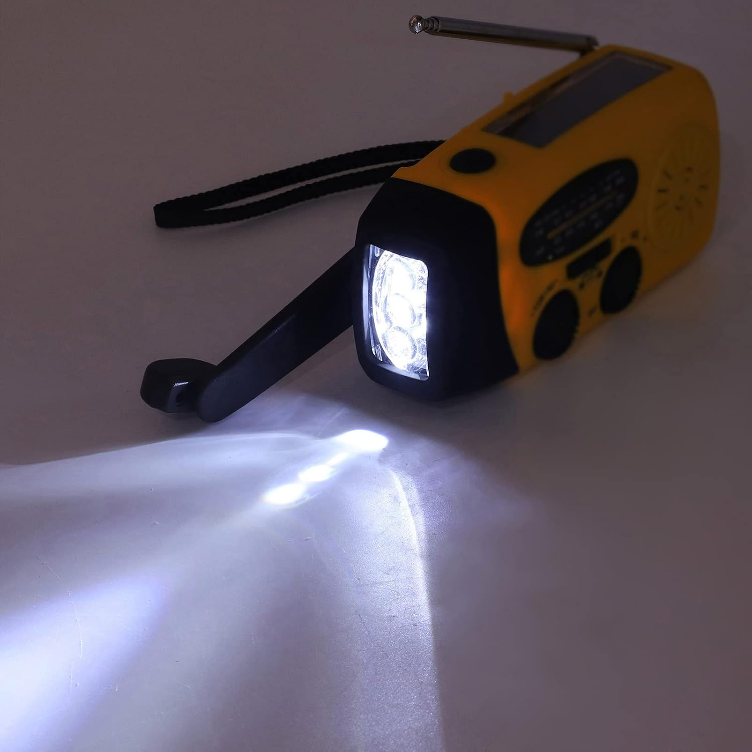 Ein gelb-schwarzes Kurbel-Notfallradio mit eingeschalteter, hell leuchtender LED-Taschenlampe, die einen Lichtkegel wirft.