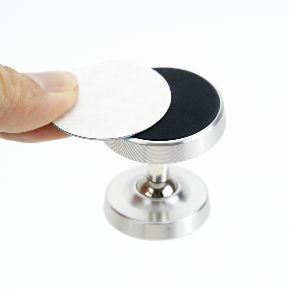 Eine Hand hält eine runde Metallplatte über eine silberne Magnethalterung auf weißem Hintergrund.