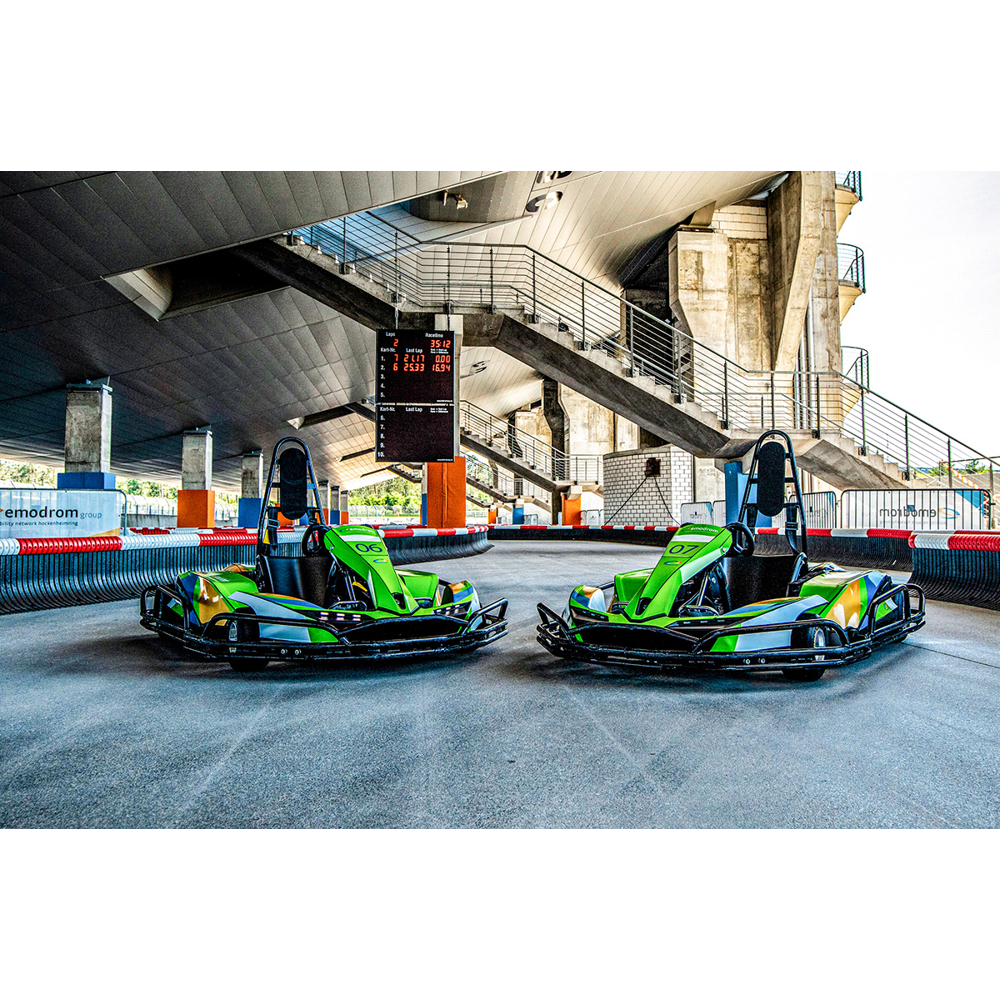 Zwei grüne Go-Karts stehen nebeneinander auf einer Rennstrecke unter einem großen Betongebäude mit Treppen.
