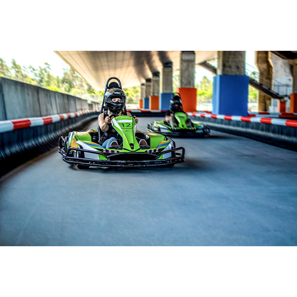 Eine Frau fährt ein grünes Go-Kart auf einer überdachten Rennstrecke, gefolgt von einem weiteren Go-Kart.