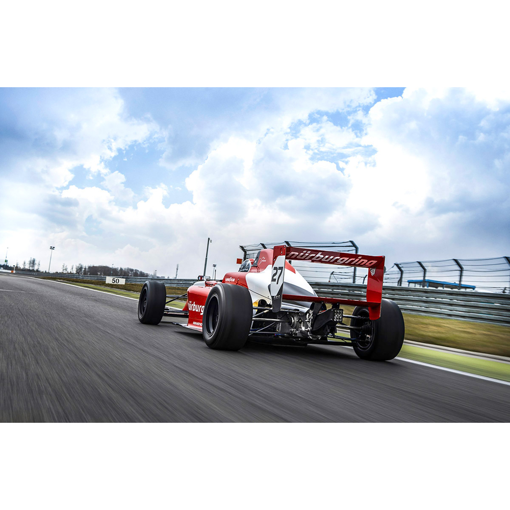 Ein roter Formel-1-Rennwagen fährt auf einer Rennstrecke unter einem bewölkten Himmel.