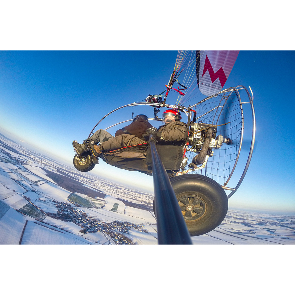 Zwei Personen fliegen im Motorschirm über eine schneebedeckte Winterlandschaft.