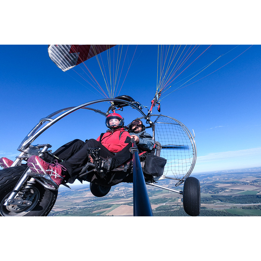 Zwei Personen fliegen in einem Motorschirm über eine weite Landschaft bei klarem blauem Himmel.