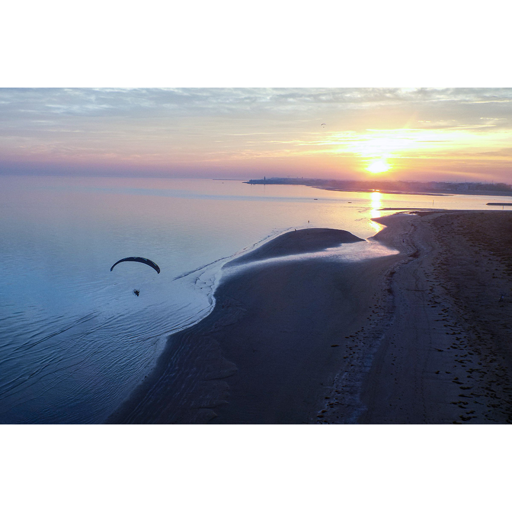 Ein Motorschirm fliegt bei Sonnenuntergang über einem ruhigen Meer und einer Küstenlinie.