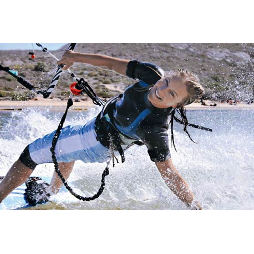 Eine Frau in Neoprenanzug und Shorts macht Kitesurfen auf blauem Wasser und sprüht Gischt.