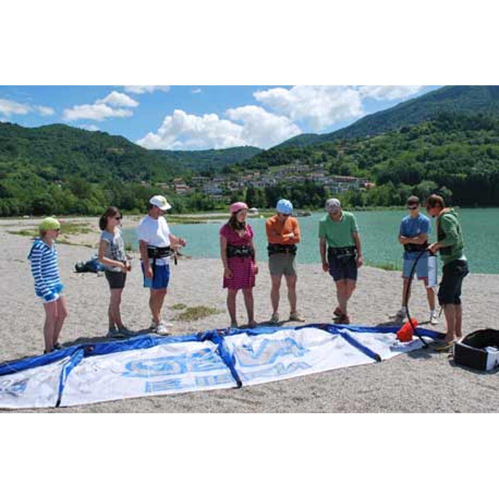 Gruppe von Menschen steht an einem See bei Vorbereitungen für Wassersport mit grünem Bergpanorama im Hintergrund.
