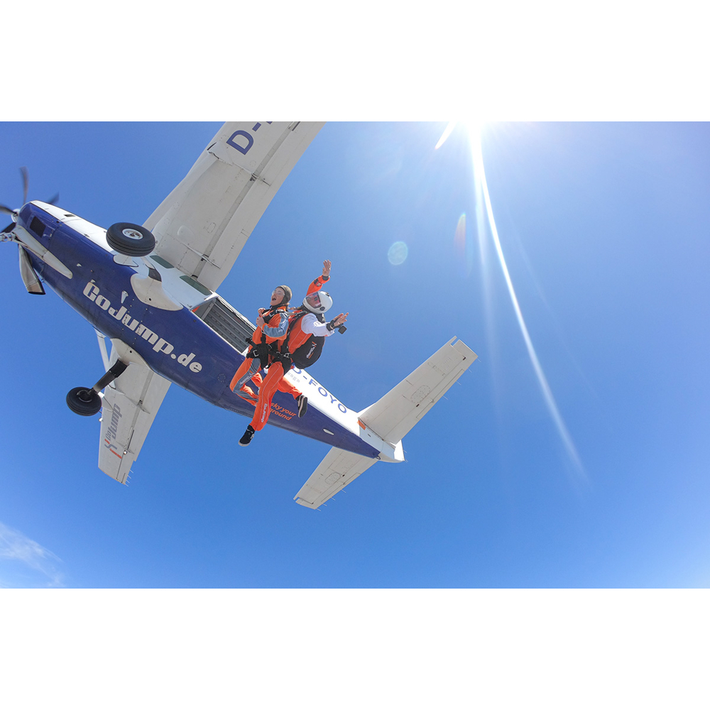 Zwei Fallschirmspringer springen vor einem blauen Himmel aus einem Flugzeug mit der Aufschrift GoJump.