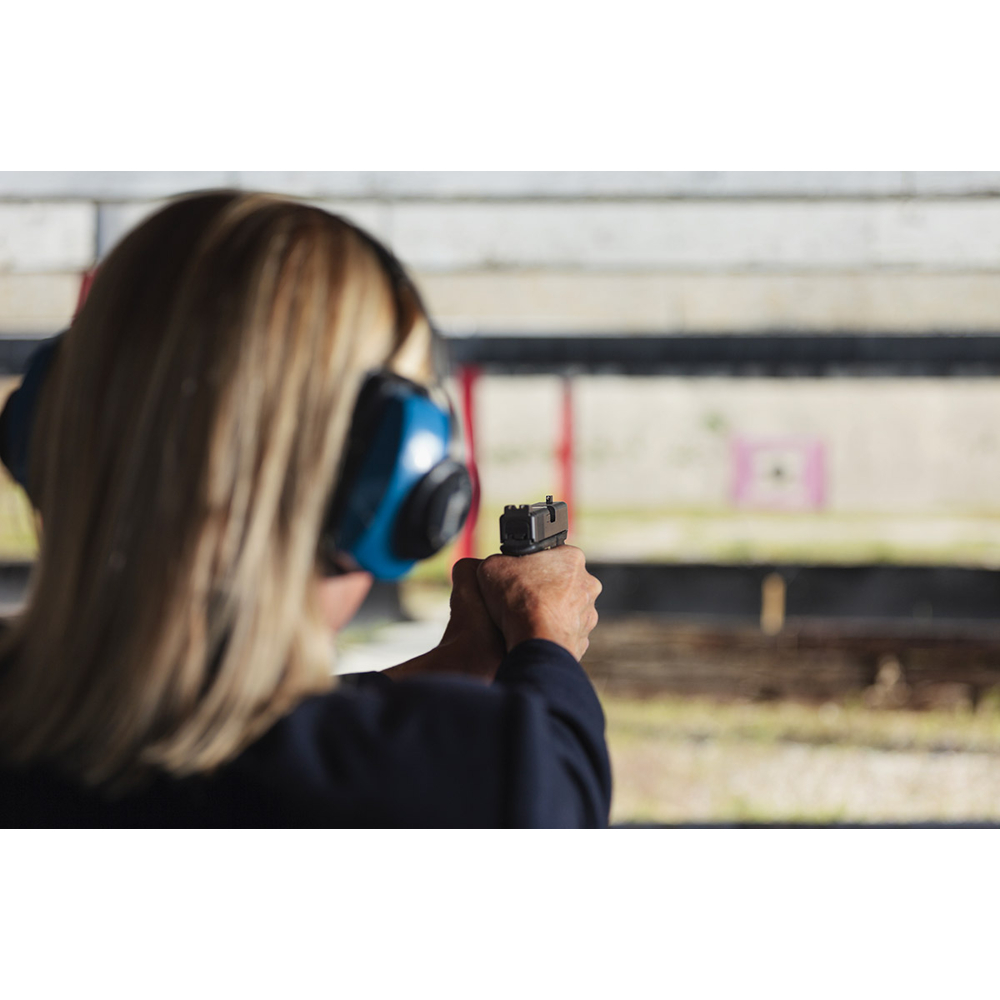 Blonde Frau trägt Gehörschutz und zielt mit einer Handfeuerwaffe auf einem Schießstand.